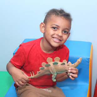 Boy with autism holds toy dinosaur and smiles