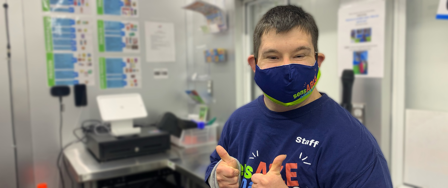 SensABLE Snacks employee smiles with mask on with two thumbs up